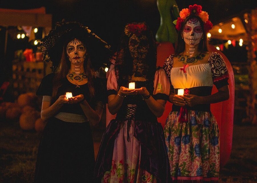 Mujeres maquilladas como catrinas y sosteniendo velas